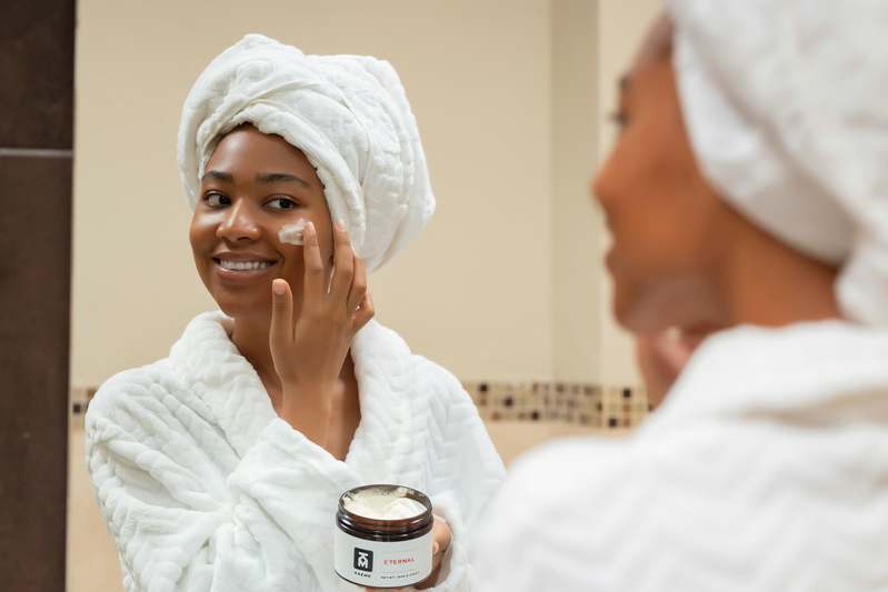Woman applying skincare while zinc supplement bottle sits on marble surface